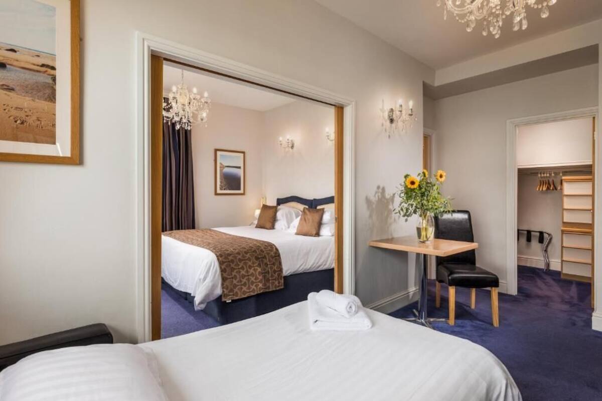 A hotel room with a large bed, a desk with a chair, a chandelier, and a closet with shelves.