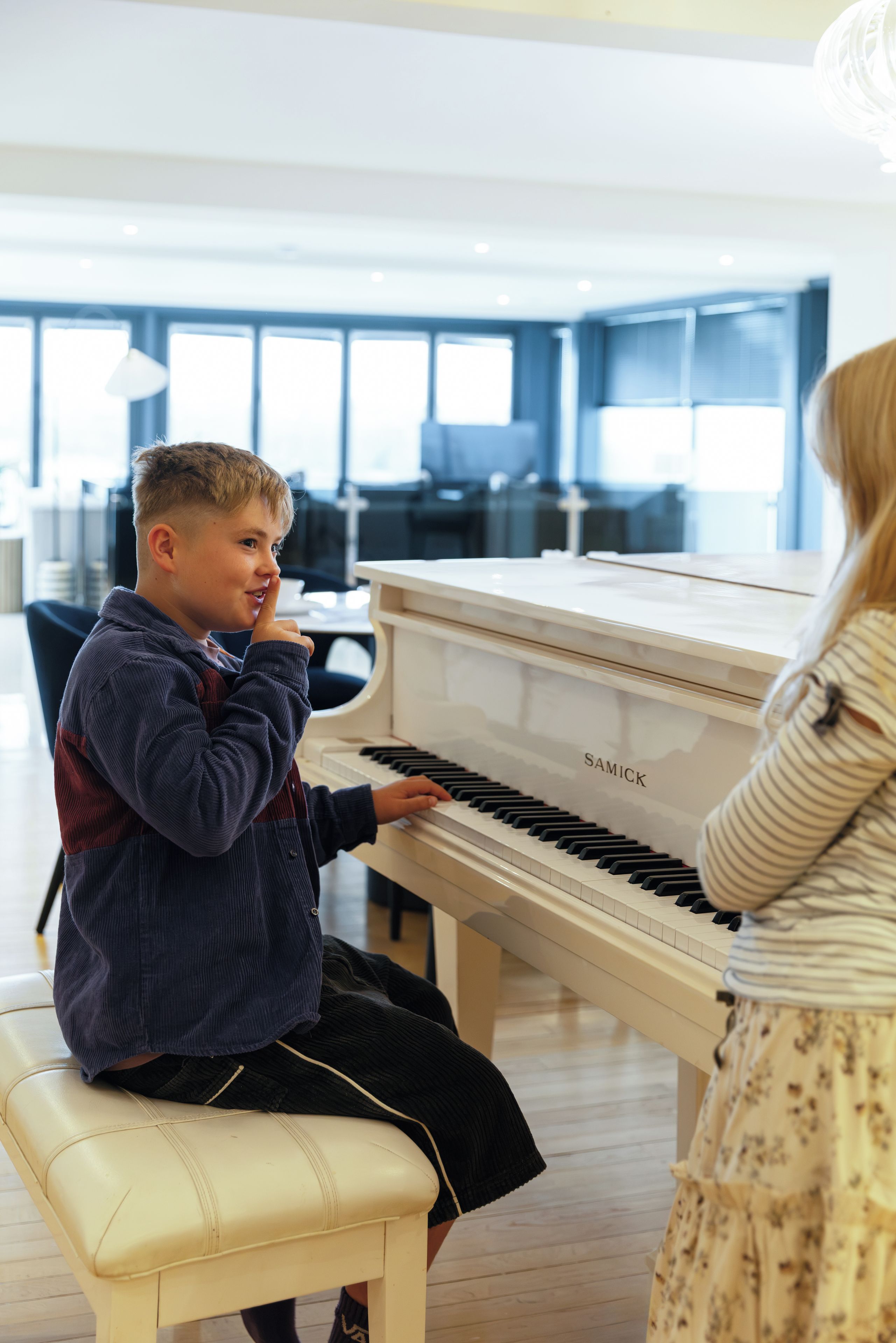 A child playing a piano in a room with large windows and modern furniture.