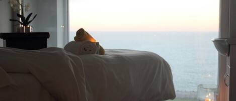 Ein Schlafzimmer mit großem Fenster, einem Bett, einem Nachttisch und einer Kerze.