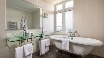 Une salle de bain moderne avec un lavabo en verre, deux porte-serviettes, une baignoire sur pieds et un grand miroir.