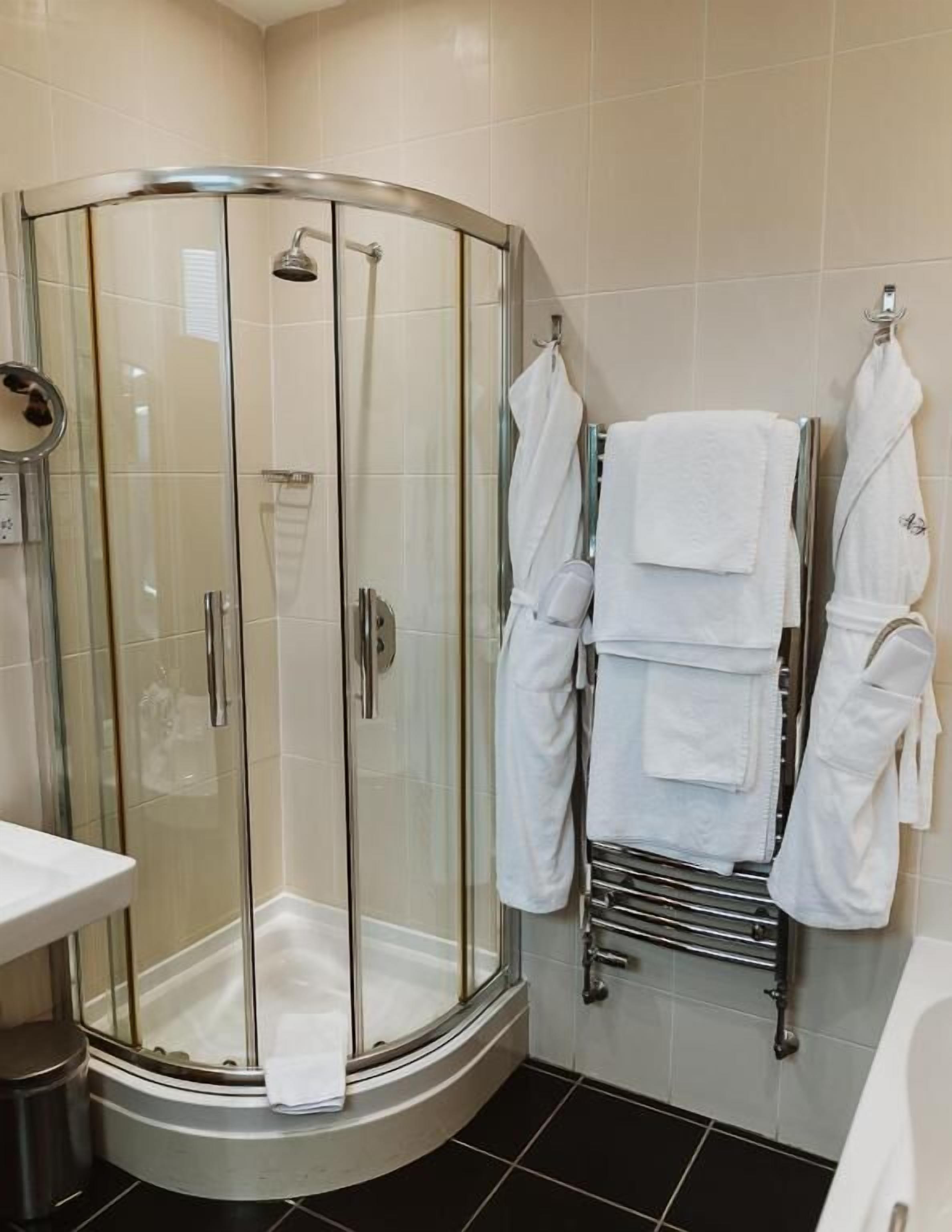 Un baño moderno con ducha de vidrio, un lavabo blanco y un perchero con varias toallas blancas.
