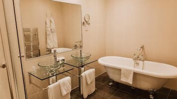 Un baño con lavamanos de cristal, una bañera independiente y un espejo sobre el lavamanos.