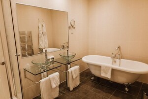 Un baño con lavamanos de cristal, una bañera independiente y un espejo sobre el lavamanos.