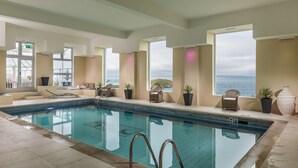 An indoor swimming pool with clear views of the sea, lounge chairs, and potted plants. - The Atlantic Hotel (Newquay)