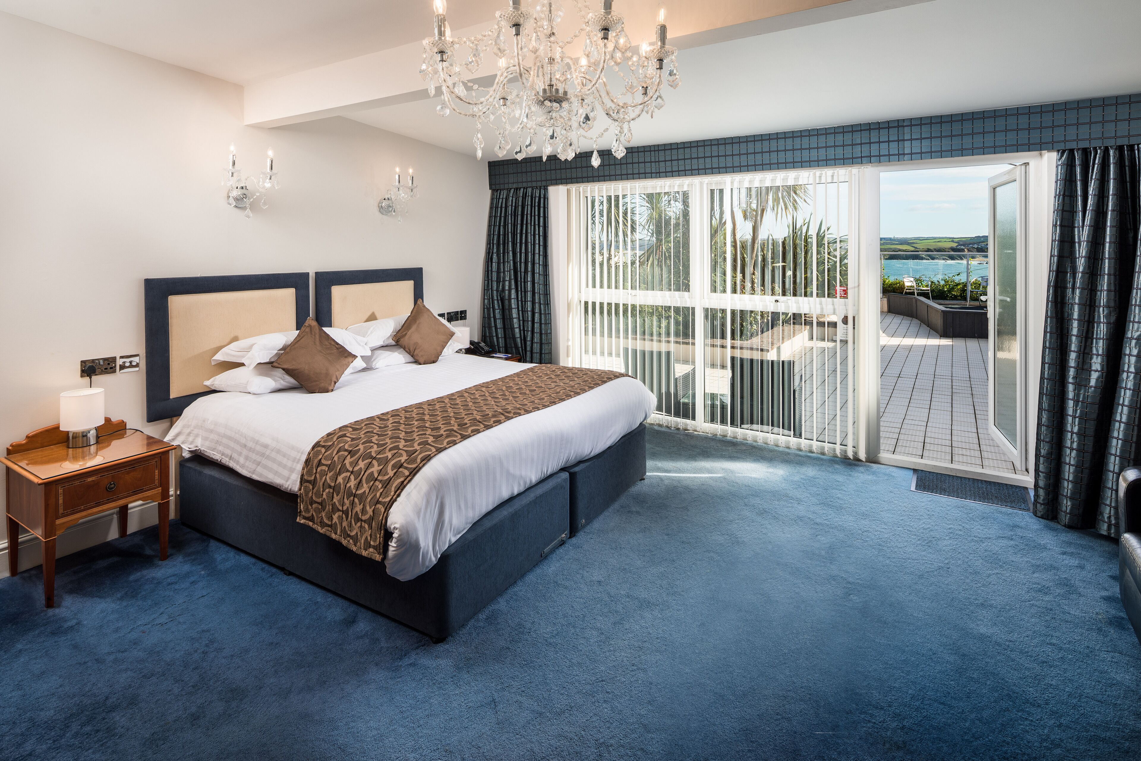 A spacious bedroom with a large bed, a chandelier, and a balcony with a view.