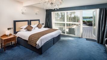 A spacious bedroom with a large bed, a chandelier, and a balcony with a view.