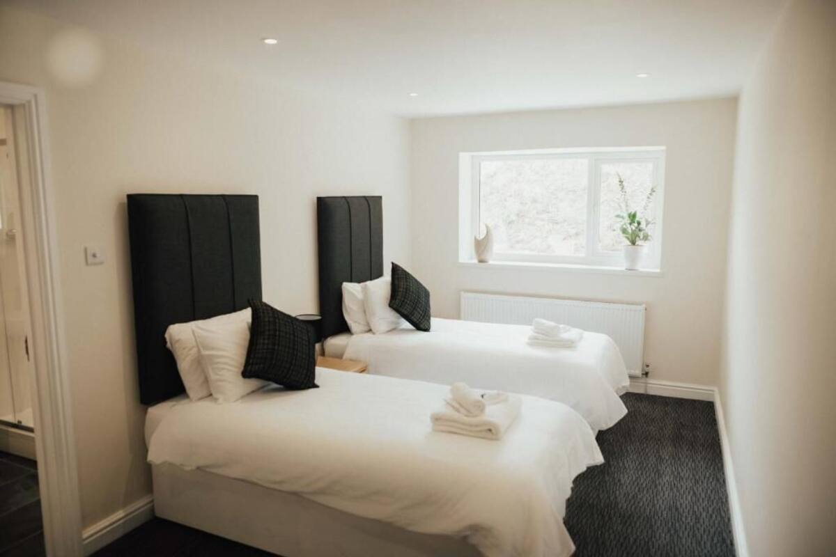 A hotel room with two beds, white bedding, dark headboards, a window with a view, and a radiator.