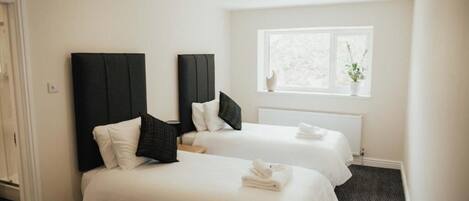 A hotel room with two beds, white bedding, dark headboards, a window with a view, and a radiator.