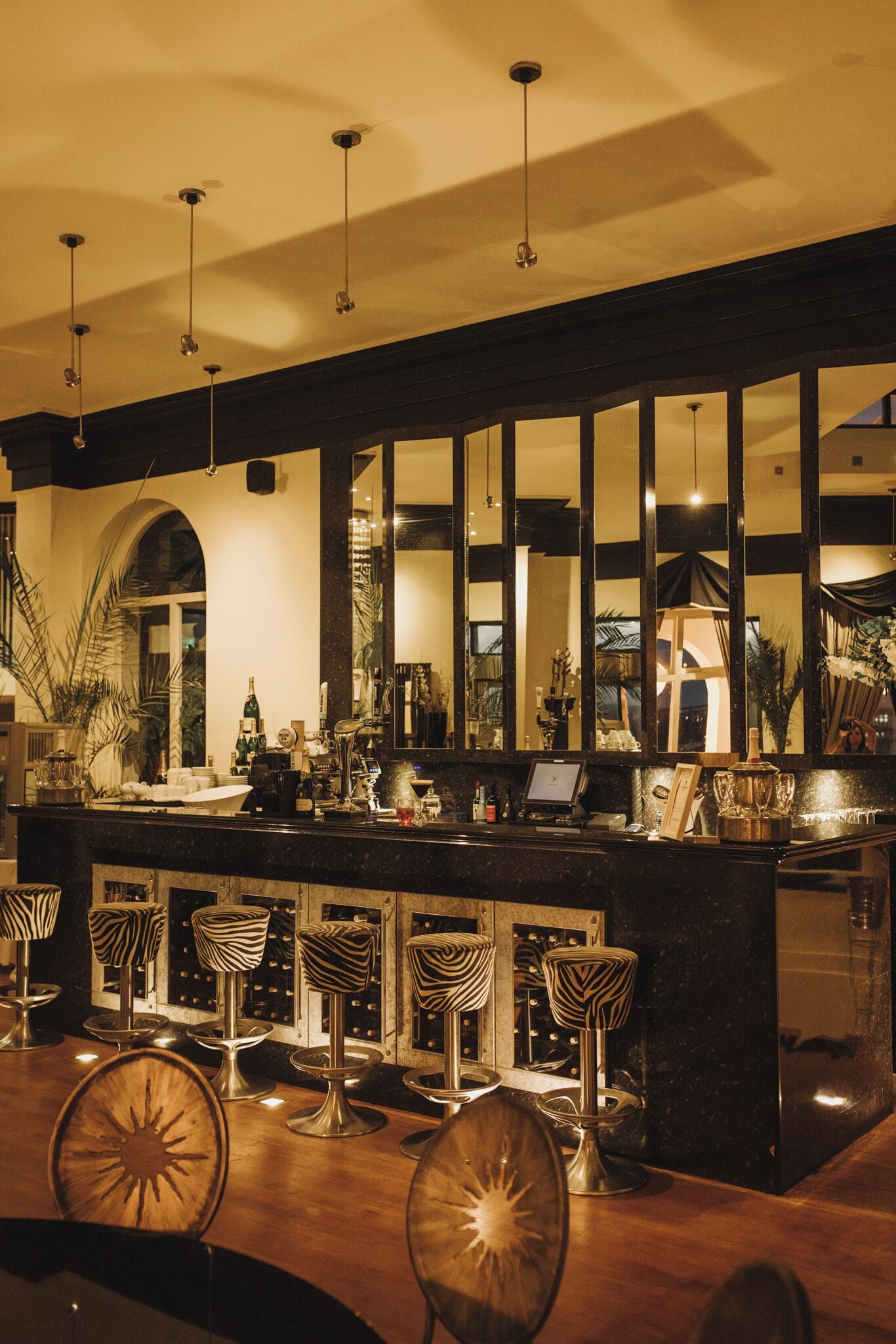 A bar area with a long counter, multiple stools, and hanging lights.
