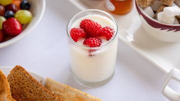 A breakfast setting with a glass of yogurt topped with raspberries, a bowl of mixed berries, and a jar of honey.