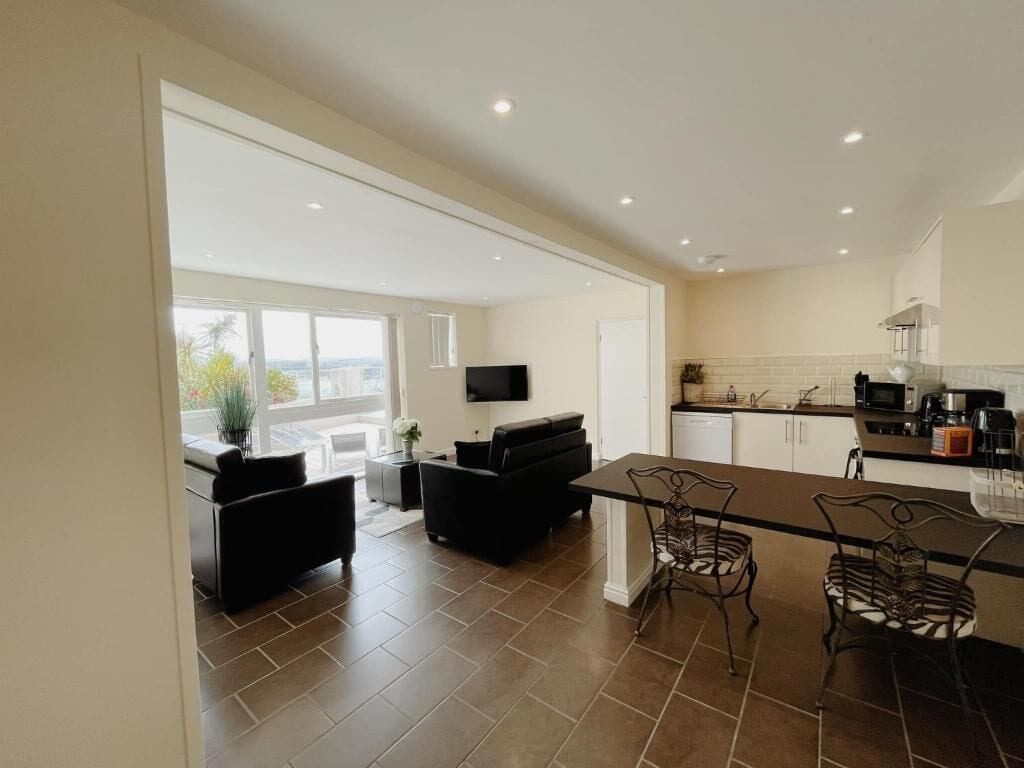 A modern kitchen with a dining area, a TV mounted on the wall, and a view of the outdoors.