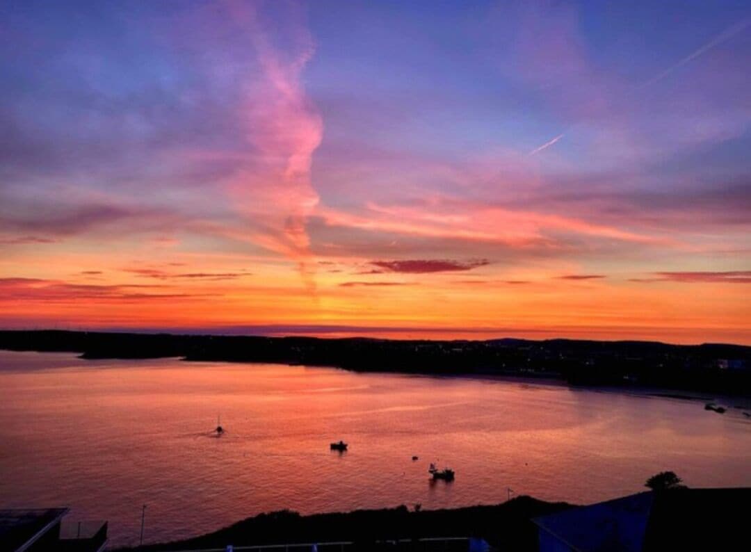 Ein Sonnenuntergang über ruhigem Gewässer mit Booten und einer fernen Küste.