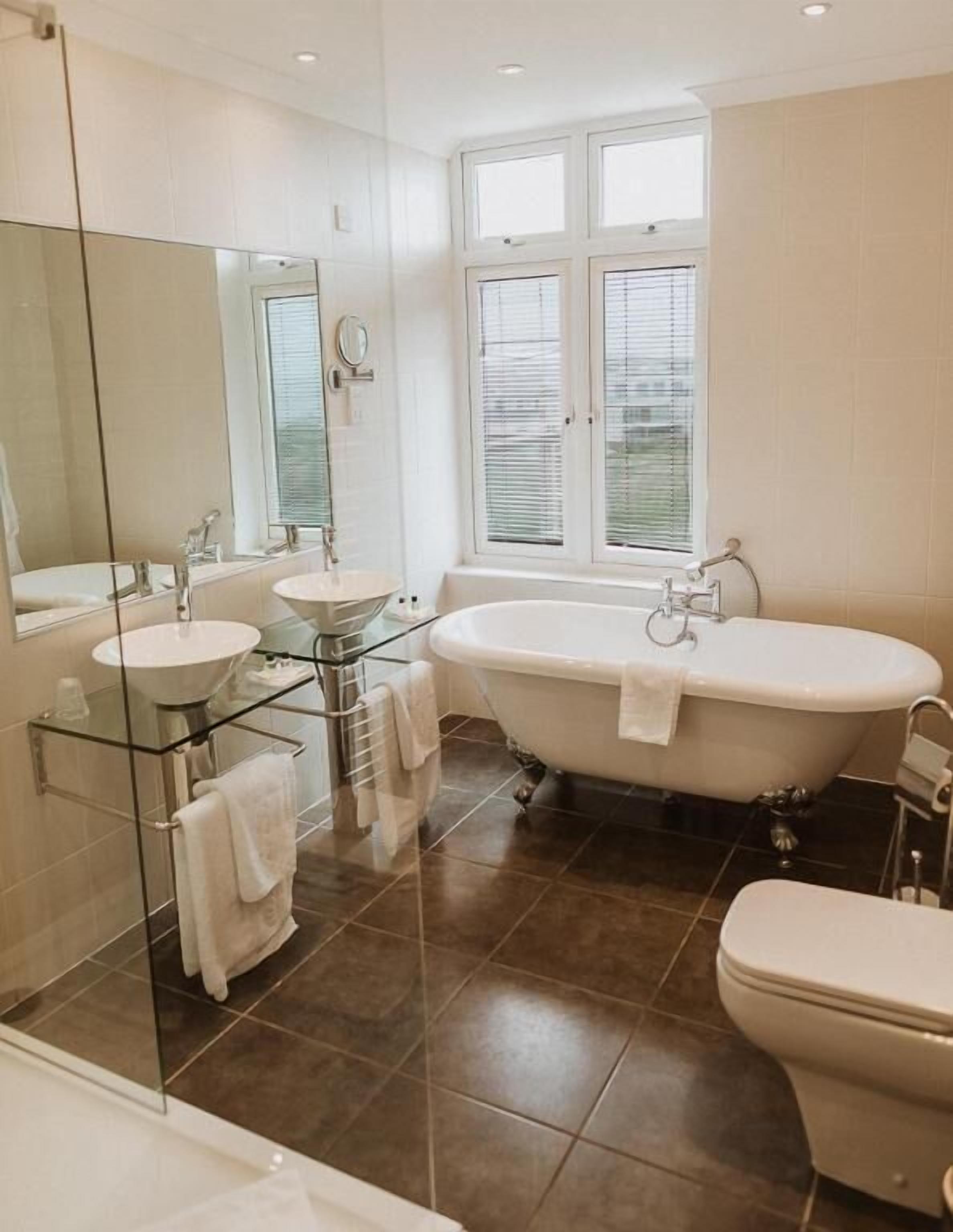 A modern bathroom with a freestanding bathtub, two sinks, a glass shower enclosure, and a large mirror.