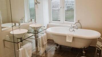 A modern bathroom with a freestanding bathtub, two sinks, a glass shower enclosure, and a large mirror.