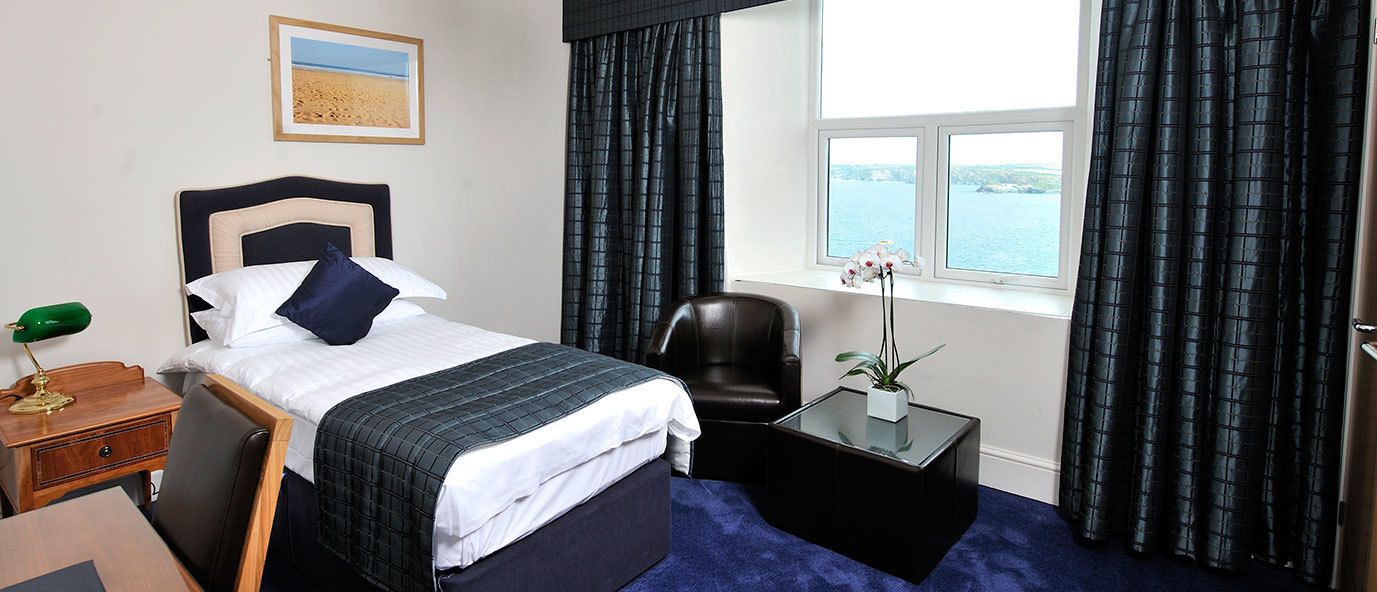 Une chambre d’hôtel avec un lit, un bureau, une chaise, une fenêtre avec des rideaux et une vue sur la mer.
