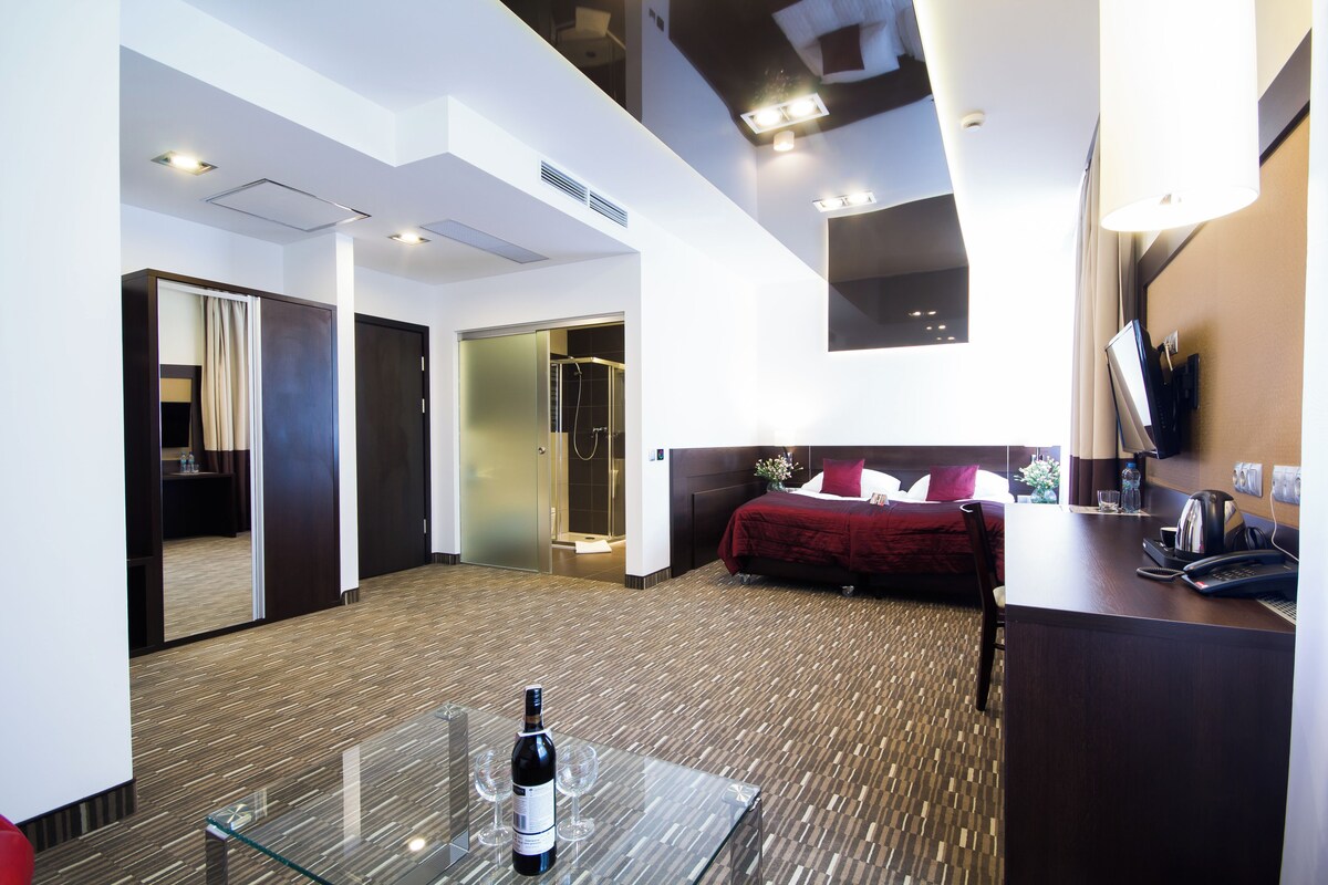 Ein Hotelzimmer mit Bett, Schreibtisch mit Telefon, Glastisch mit Flasche und Gläsern sowie einem Spiegel an der Wand.