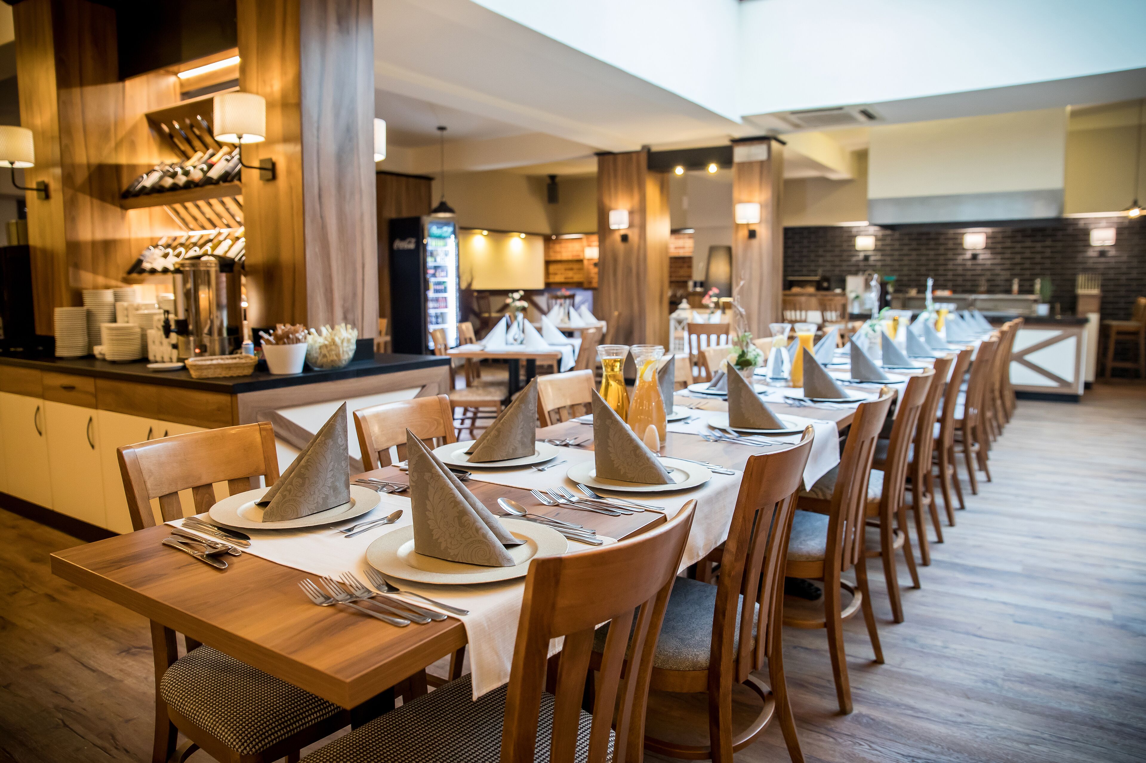 A restaurant with long wooden tables set for dining, featuring napkins and cutlery.