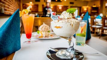 Dessert mit Schlagsahne und einem Minzblatt auf einer Glasplatte.