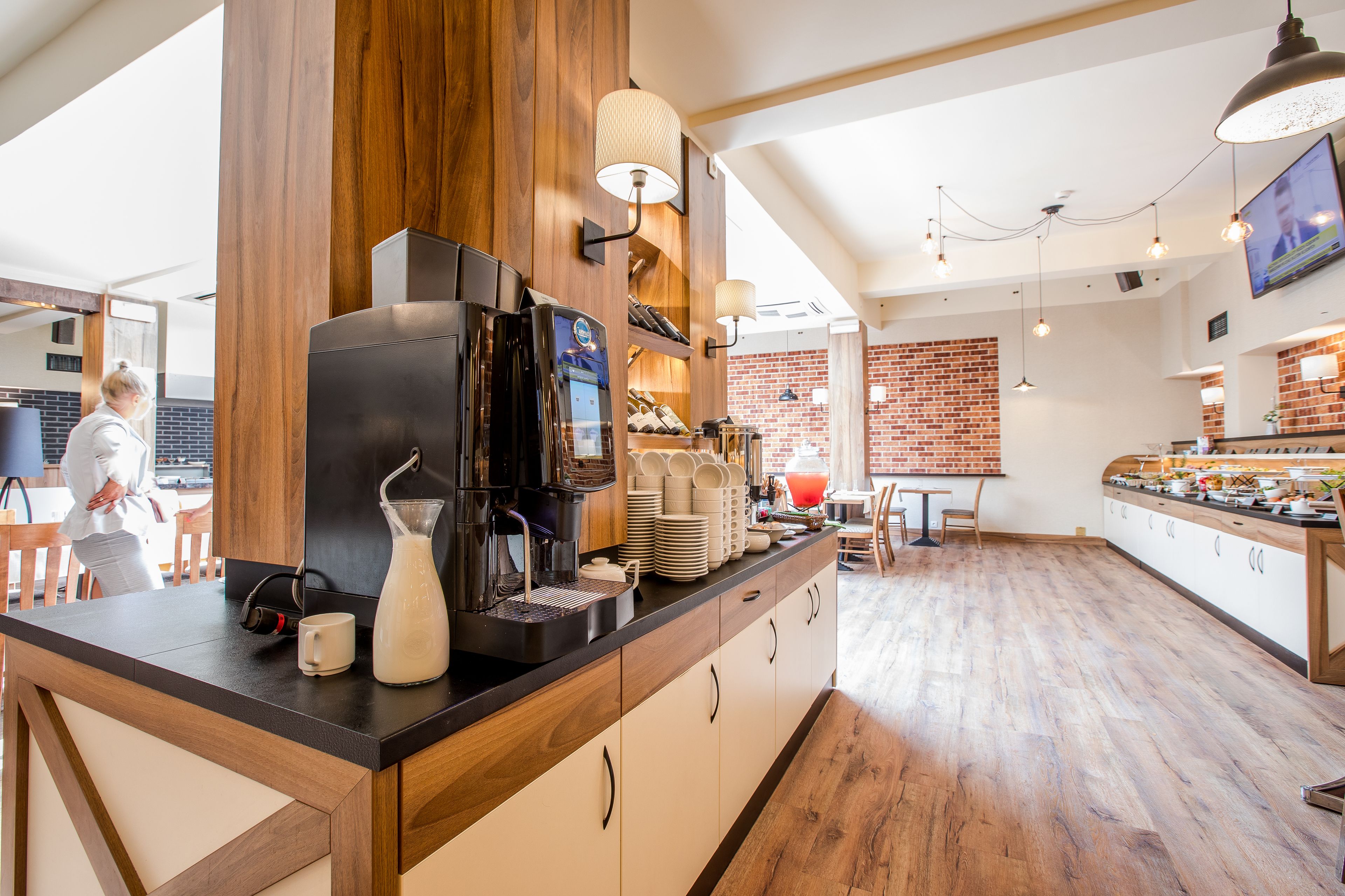 Una cocina moderna con detalles de madera, una estación de café y una pared de ladrillo al fondo.