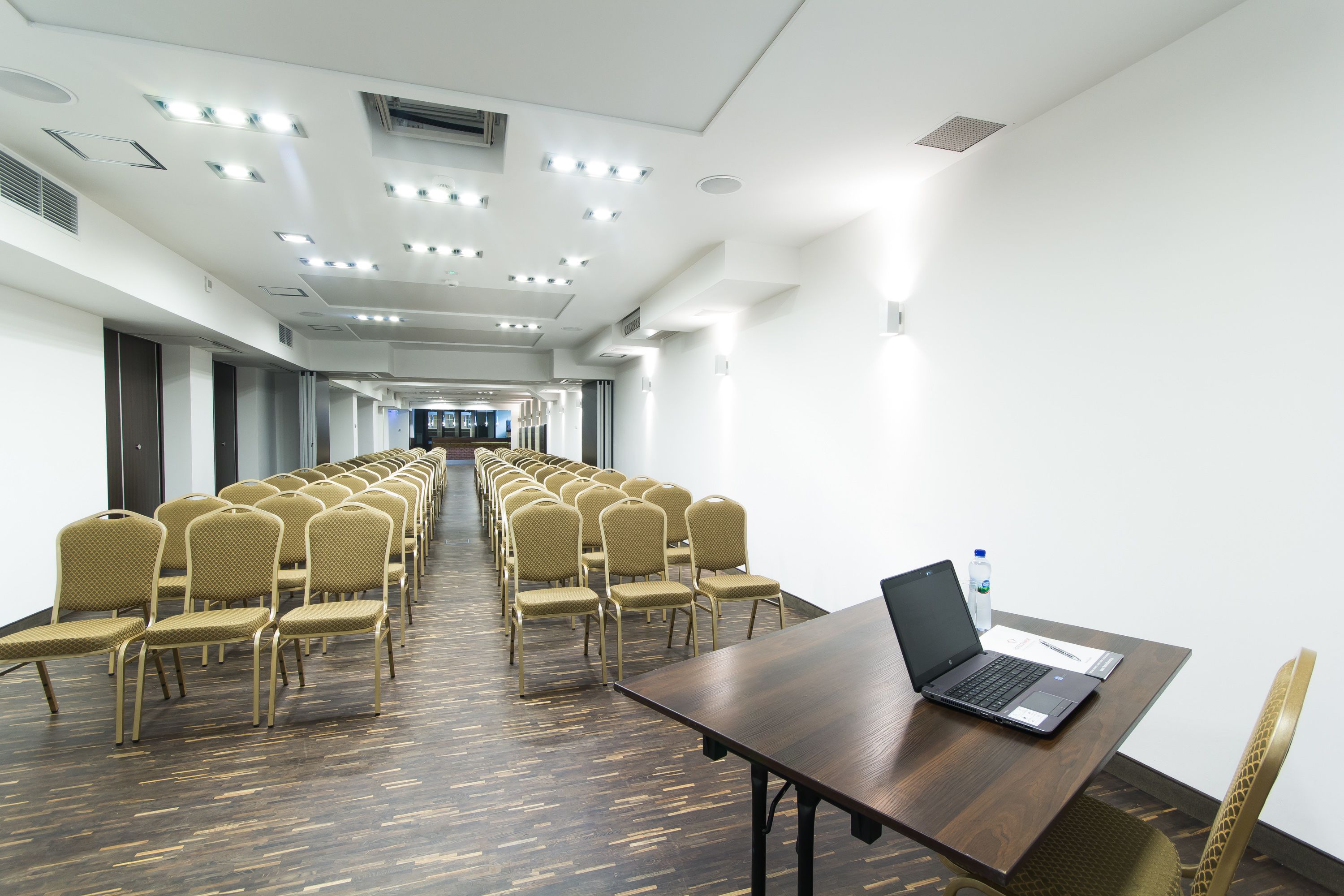 A conference room with rows of chairs, a laptop on a table, and a water bottle.