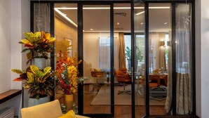 Een moderne woonkamer met een glazen scheidingswand, een gele bank en een grote plant.