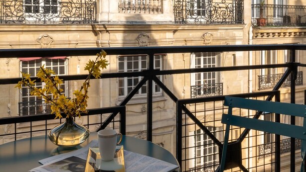 Een balkon met een tafel, een stoel, een bloevas en een krant.