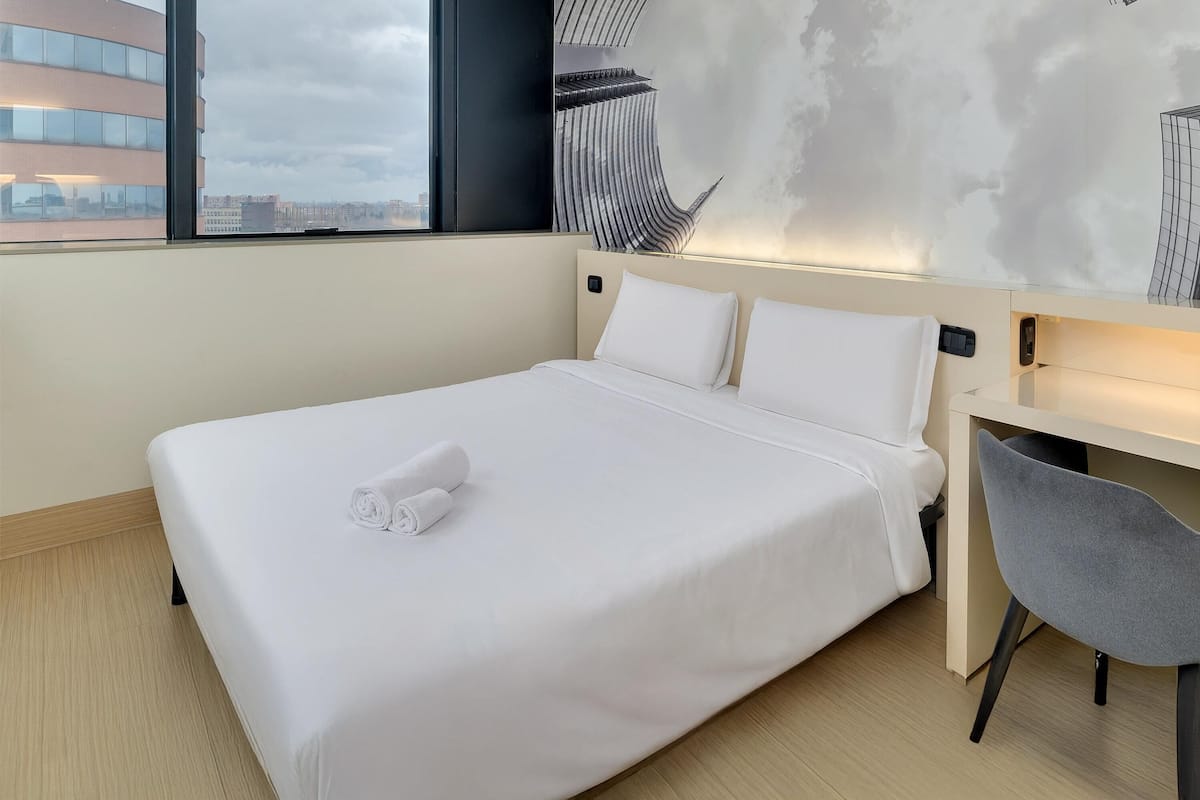 A hotel room with a bed, a desk, and a chair.