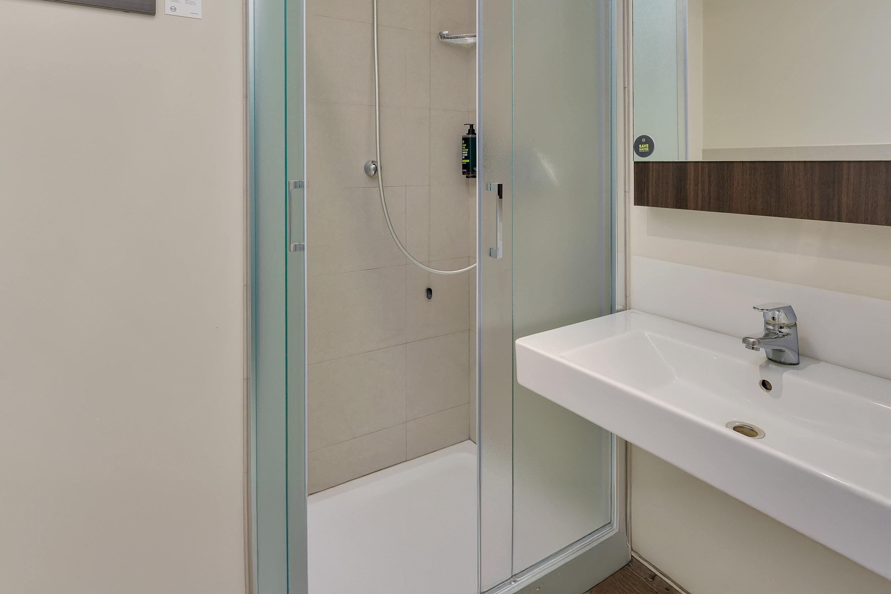 Un baño moderno con ducha de vidrio, un lavabo blanco y un espejo encima.