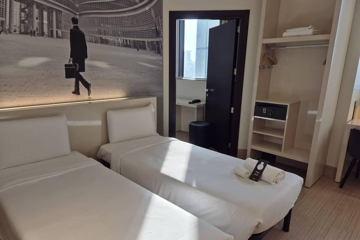 A hotel room with two beds, a desk, a wardrobe, and a large window.