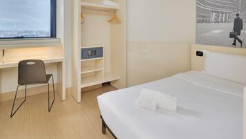A hotel room with a bed, a desk, a chair, a wardrobe, and a large window.