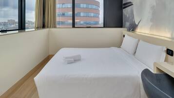 A hotel room with a large bed, a bedside table, and a view of a building through the window.