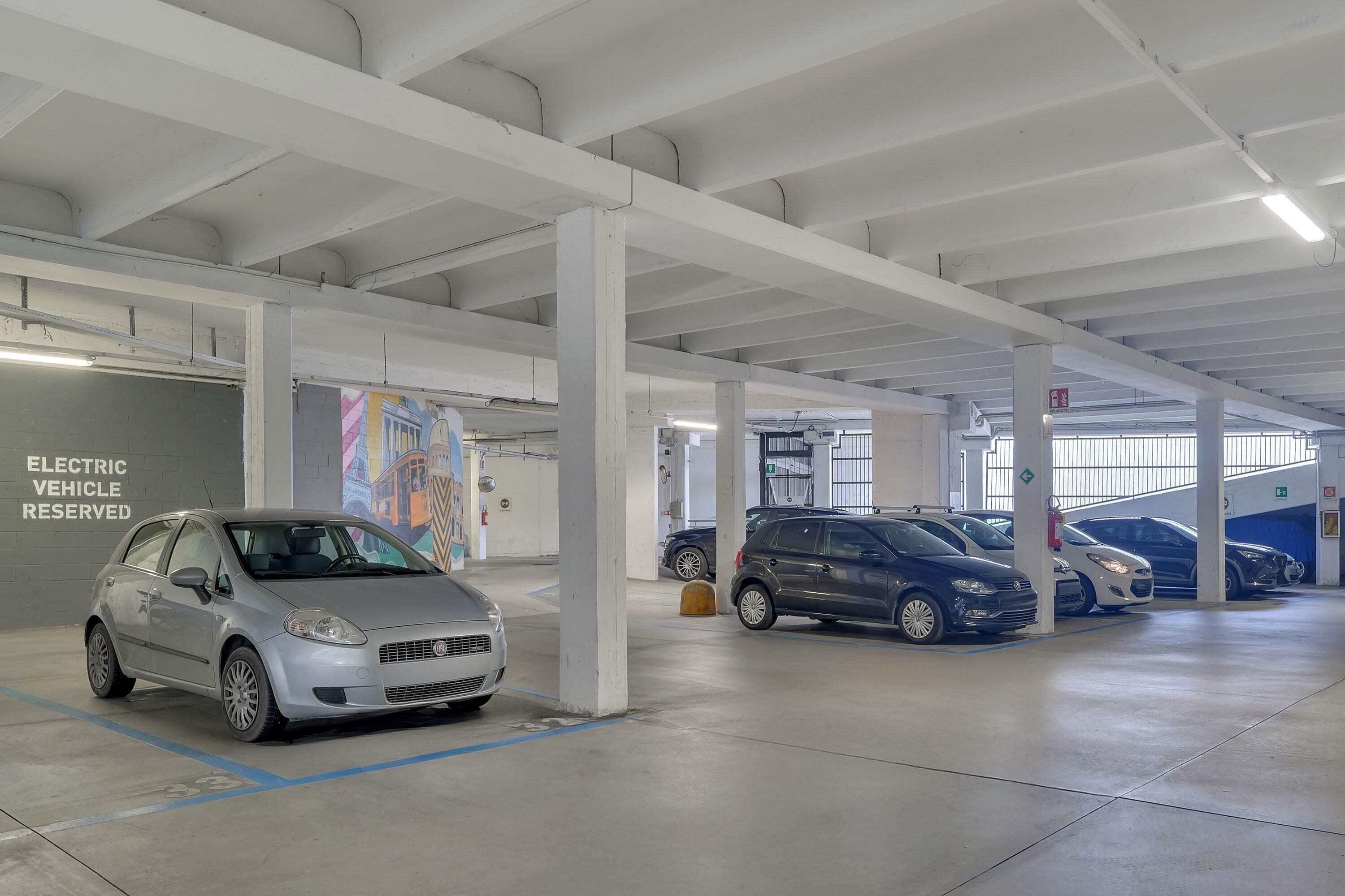 Un garaje de estacionamiento interior con pilares blancos, estaciones de carga para vehículos eléctricos y varios automóviles estacionados.