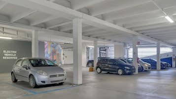 Un garaje de estacionamiento interior con pilares blancos, estaciones de carga para vehículos eléctricos y varios automóviles estacionados.