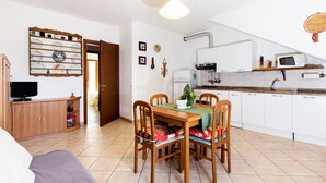 Un espacio habitable compacto con comedor, kitchenette y televisor en un rincón.