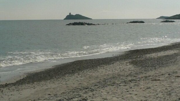 Una playa con costa pedregosa, mar tranquilo e islas rocosas a lo lejos.