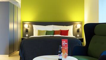 A hotel room with a bed, bedside lamps, a table with a bottle and glass, and a red sign on the wall.