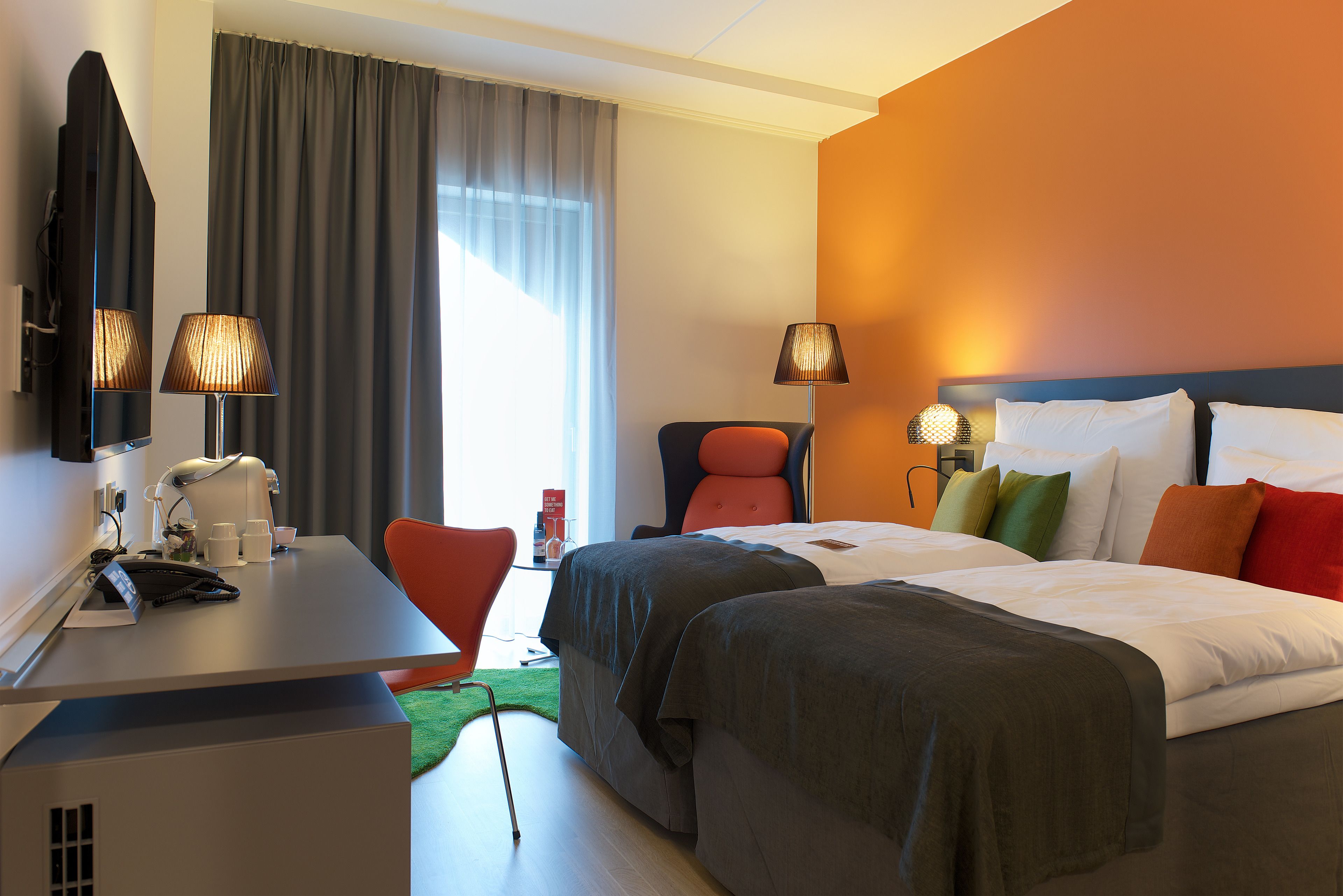 Habitación de hotel con cama, dos mesitas de noche, un escritorio, una silla, televisor y ventana con cortinas.
