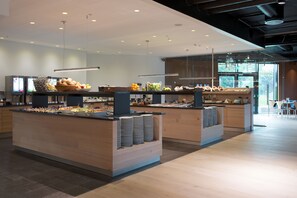 Un espace moderne dédié au petit-déjeuner, doté de plusieurs points de service, offrant une grande variété d’aliments et présentant un design épuré et contemporain.