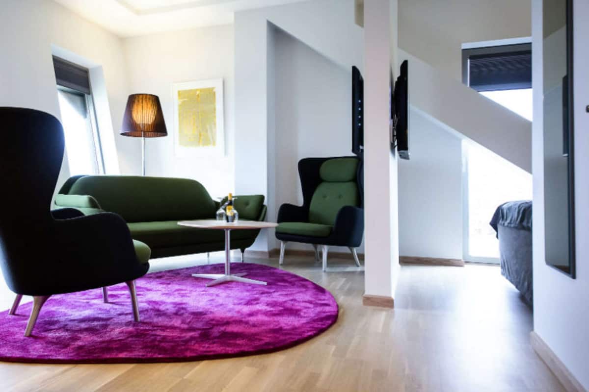 A modern living room with a green sofa, a black armchair, and a purple rug.