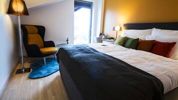 A modern hotel room with a large bed, a chair, a desk, and a lamp.