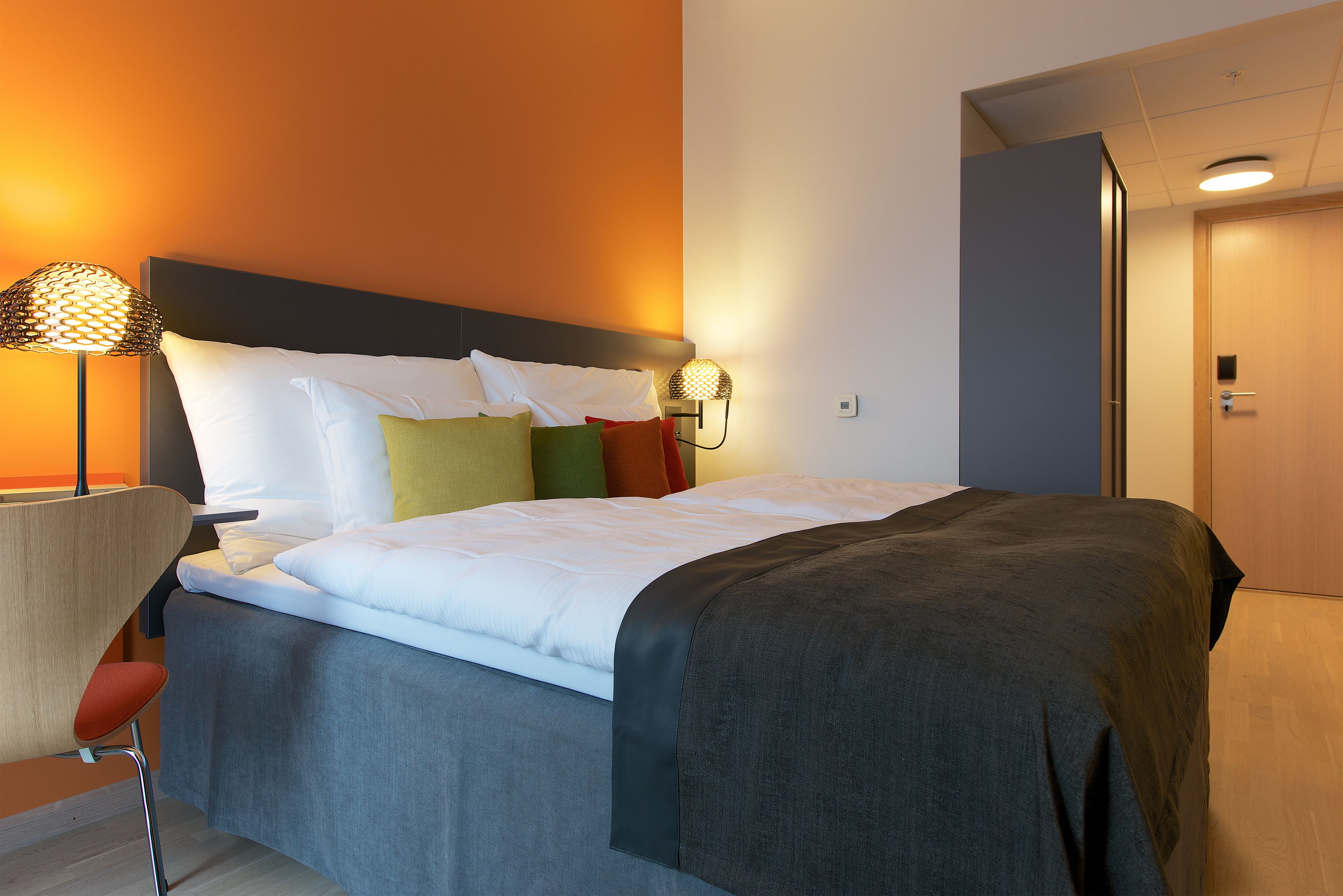 A neatly made bed with a grey and white duvet, a headboard, and a bedside lamp.