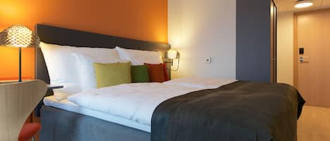 Una cama bien hecha con edredón gris y blanco, cabecera y lámpara de noche.