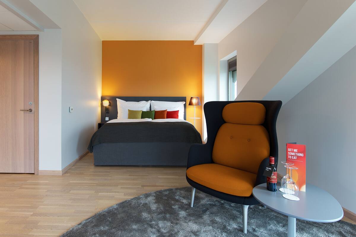 A modern bedroom with a bed, a chair, a small table with a bottle and glass, and a sign.
