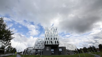 A modern hotel with a unique geometric facade, a central entrance, and a well-maintained lawn area.