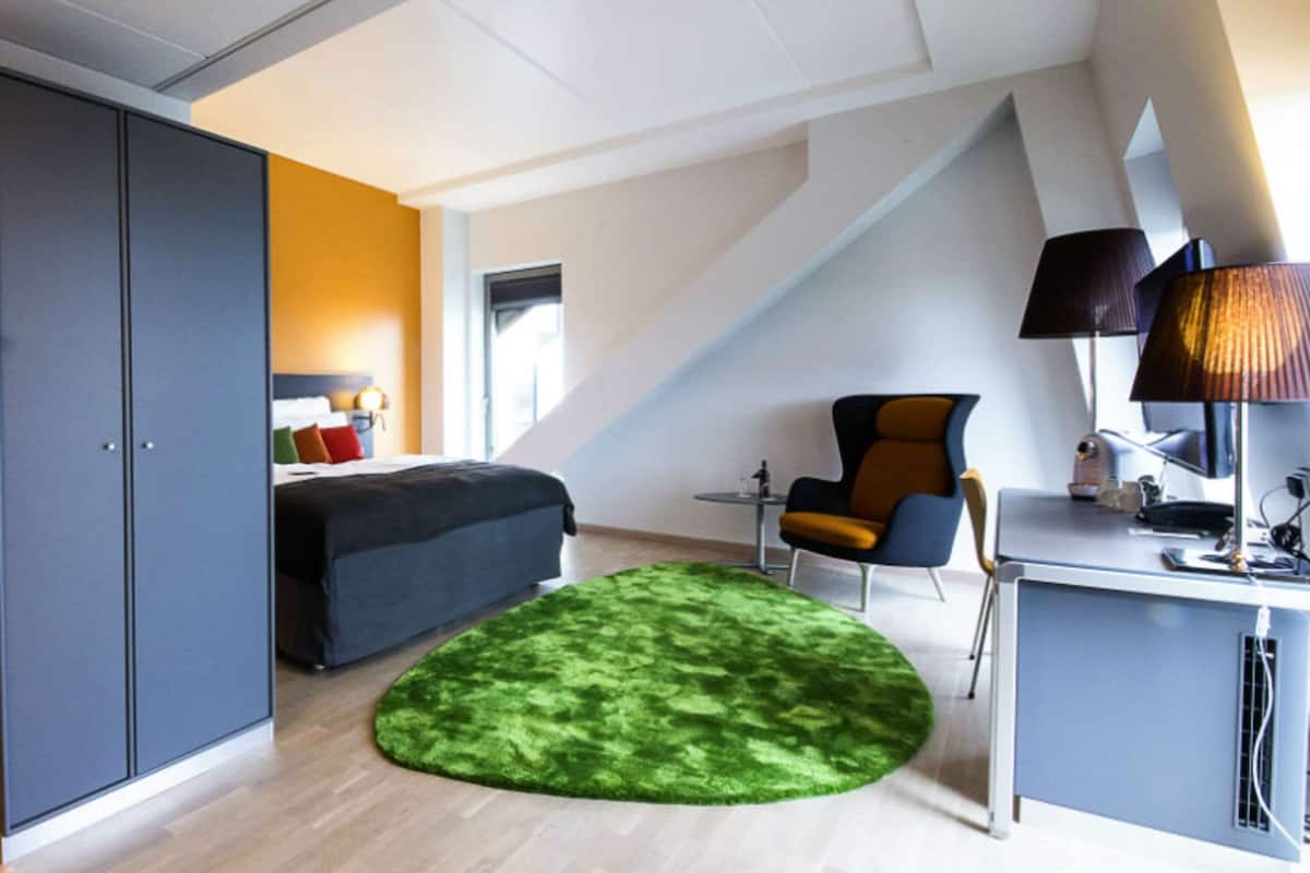 A modern bedroom with a bed, a desk, a chair, and a green rug.