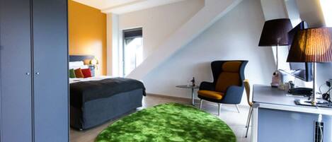 A modern bedroom with a bed, a desk, a chair, and a green rug.
