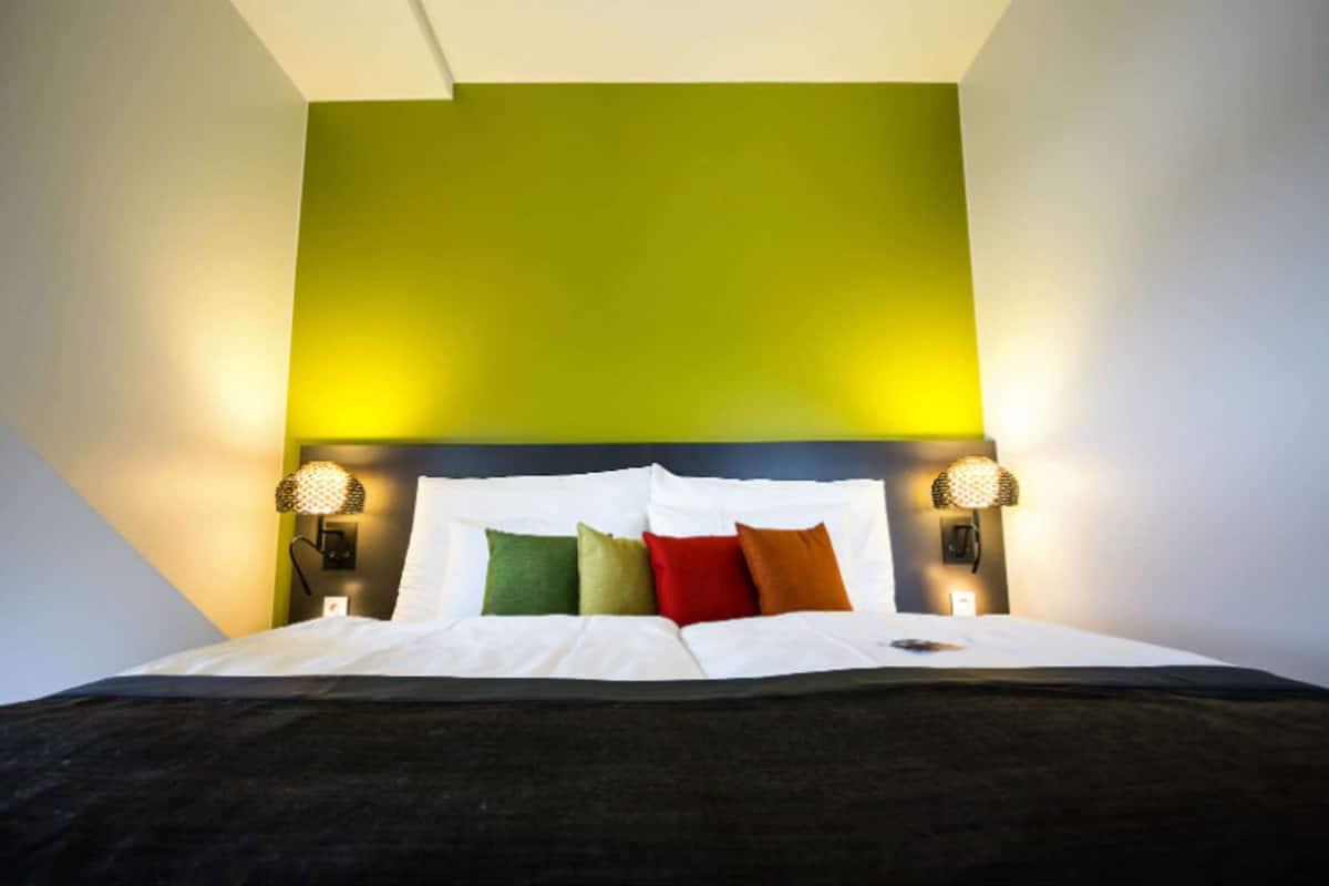 A bed with white bedding, a green accent wall, and two wall-mounted lamps.