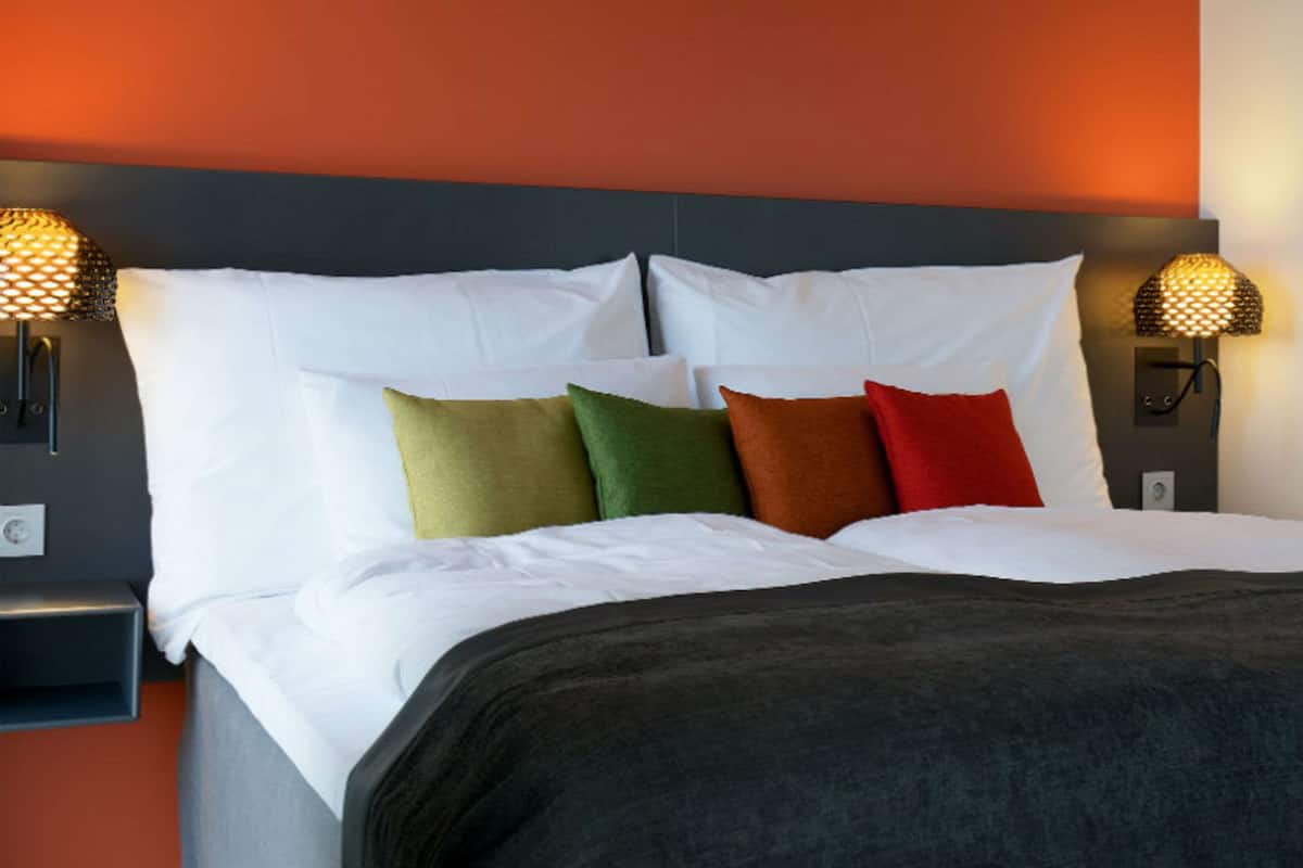 A neatly made bed with white linens and multiple pillows in various colors.
