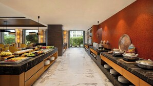 A modern hotel kitchen with marble countertops, a variety of food items, and a view of greenery outside.