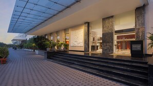 A modern hotel entrance with a glass canopy, marble columns, and a well-lit lobby area.